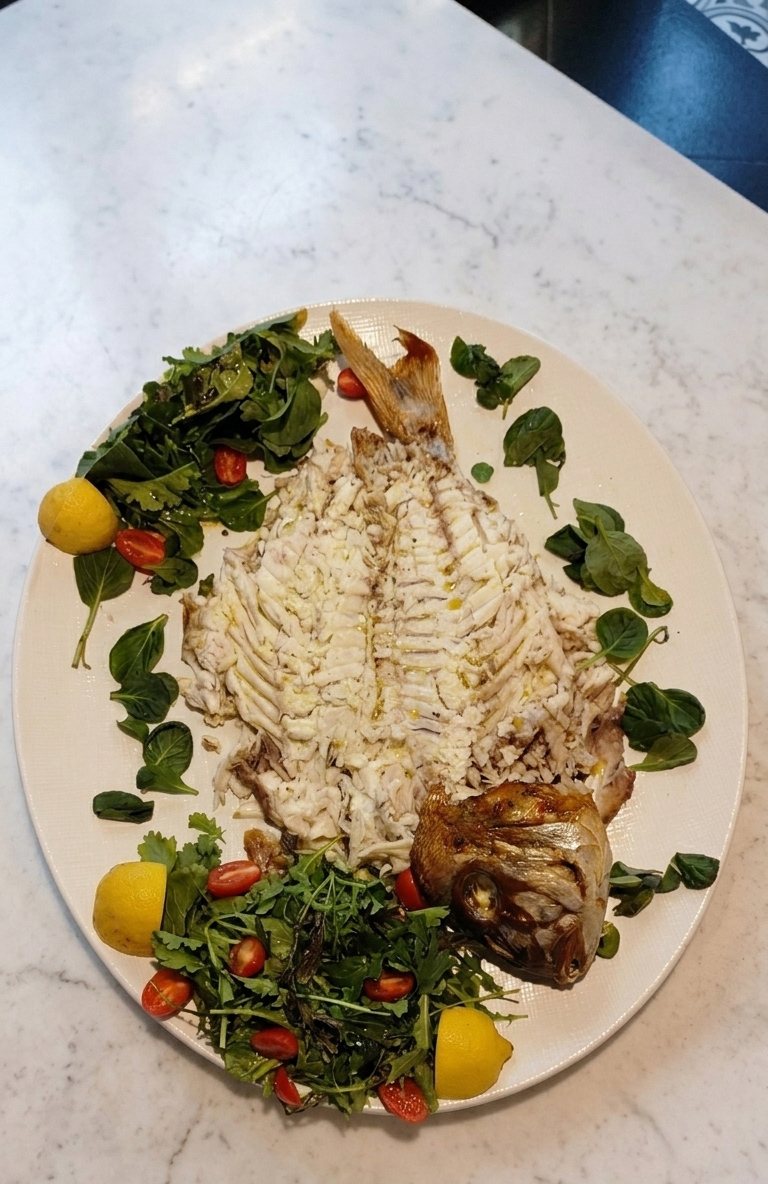 A whole grilled fish, opened and boned, served with rocket, cherry tomatoes and lemon halves