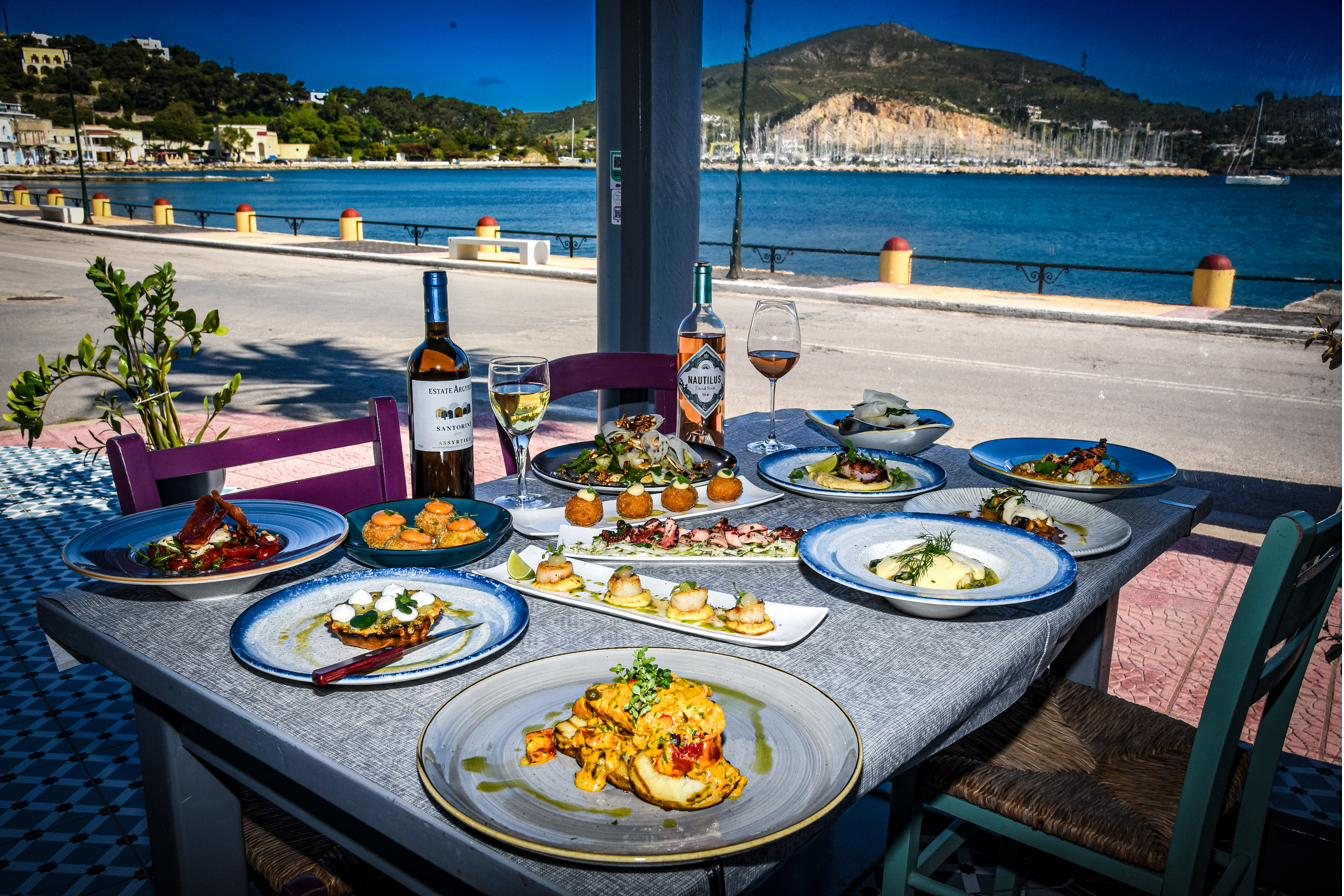 A long table of Greek meze dishes and wine on the El Greco Leros terrace, overlooking the blue water and hills of Lakki bay