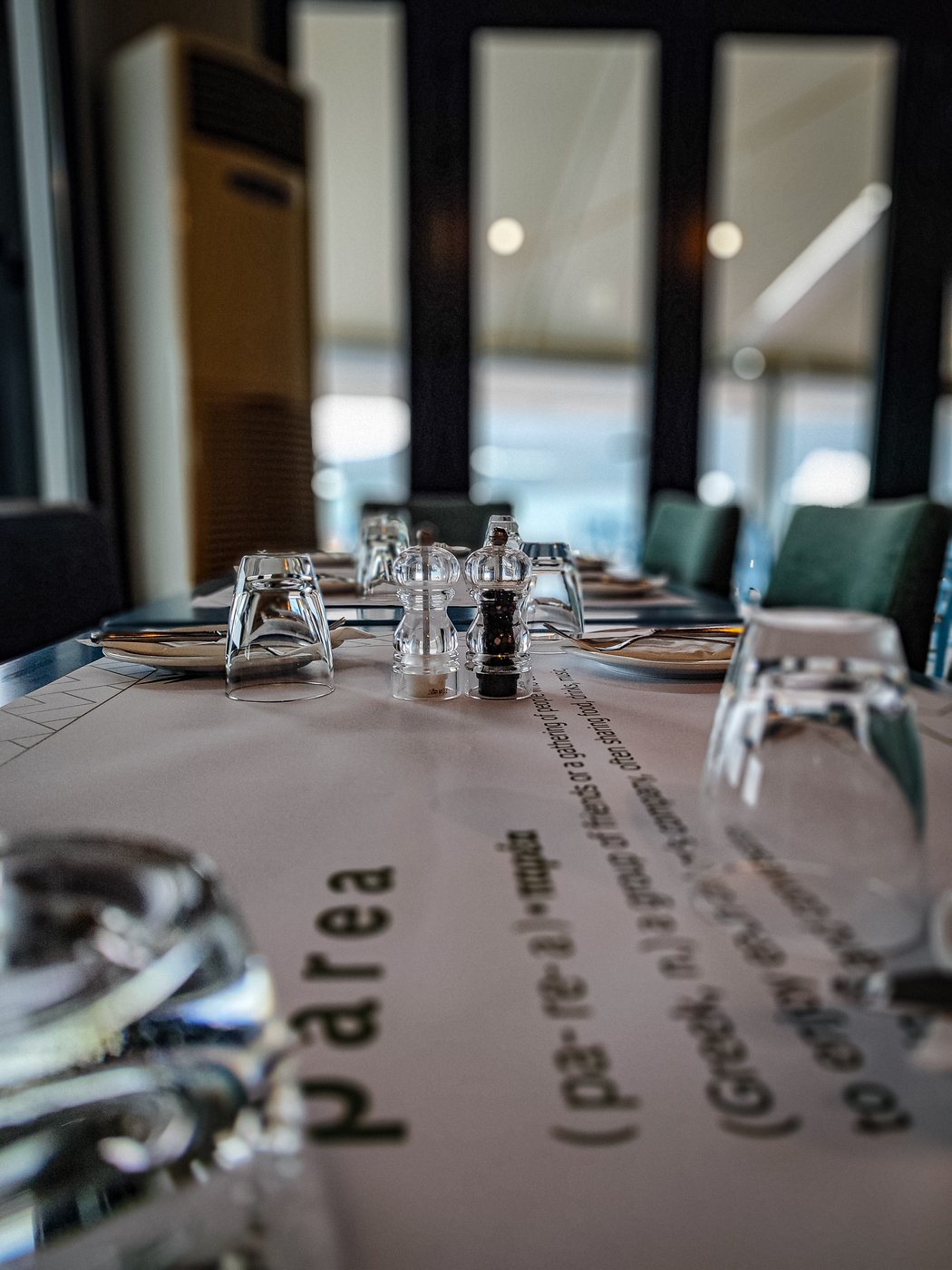 A close view of a laid table with the parea placemat, glasses and salt and pepper mills, windows behind