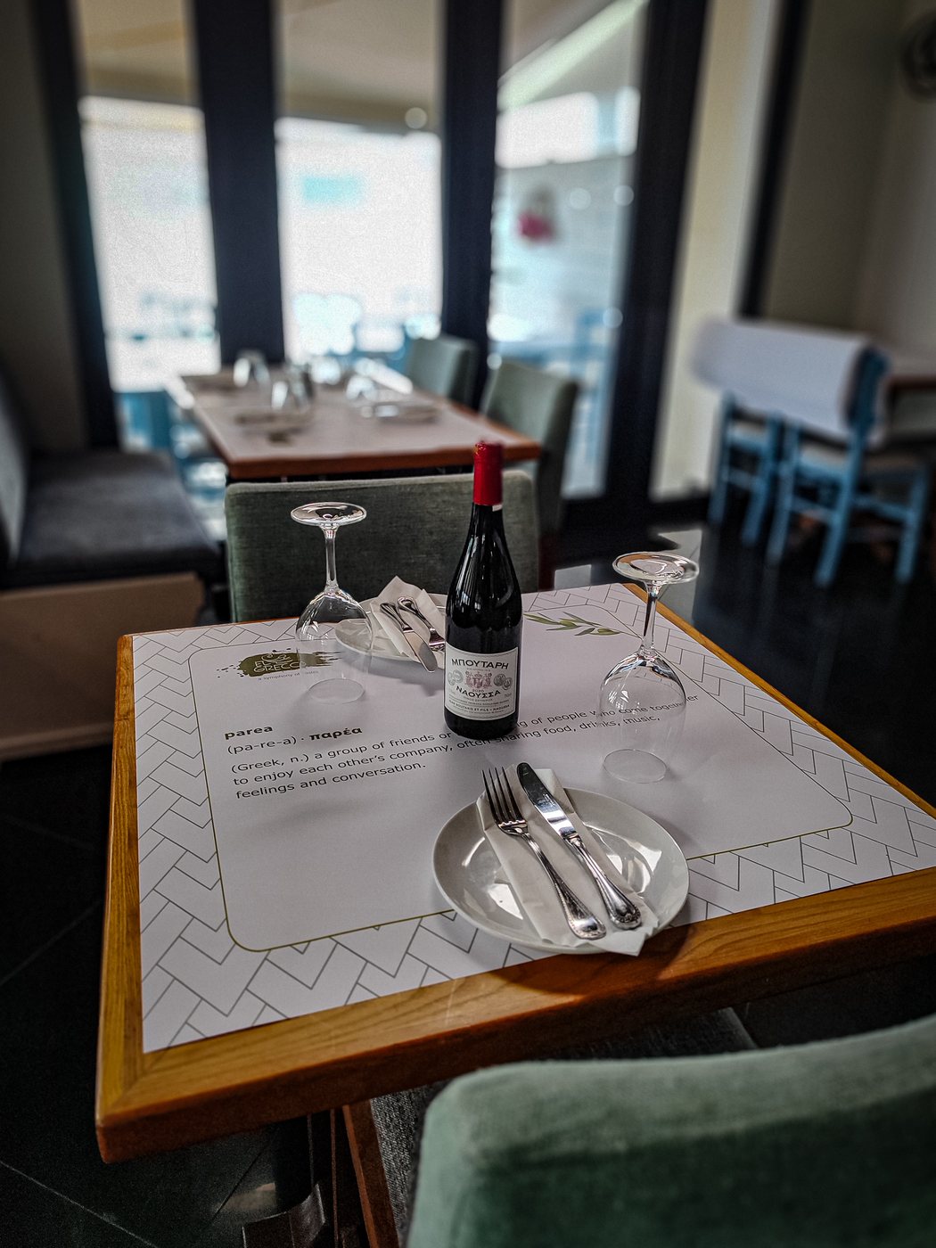 A table laid with the El Greco parea placemat, a bottle of Greek red wine and upturned glasses
